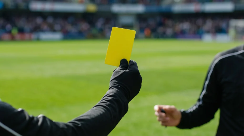 Árbitro de fútbol mostrando una tarjeta amarilla durante un partido en un campo de césped profesional
