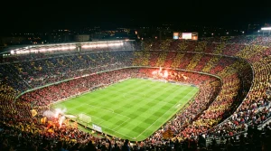 Estadio de fútbol lleno de espectadores durante un partido nocturno de LaLiga con el césped iluminado